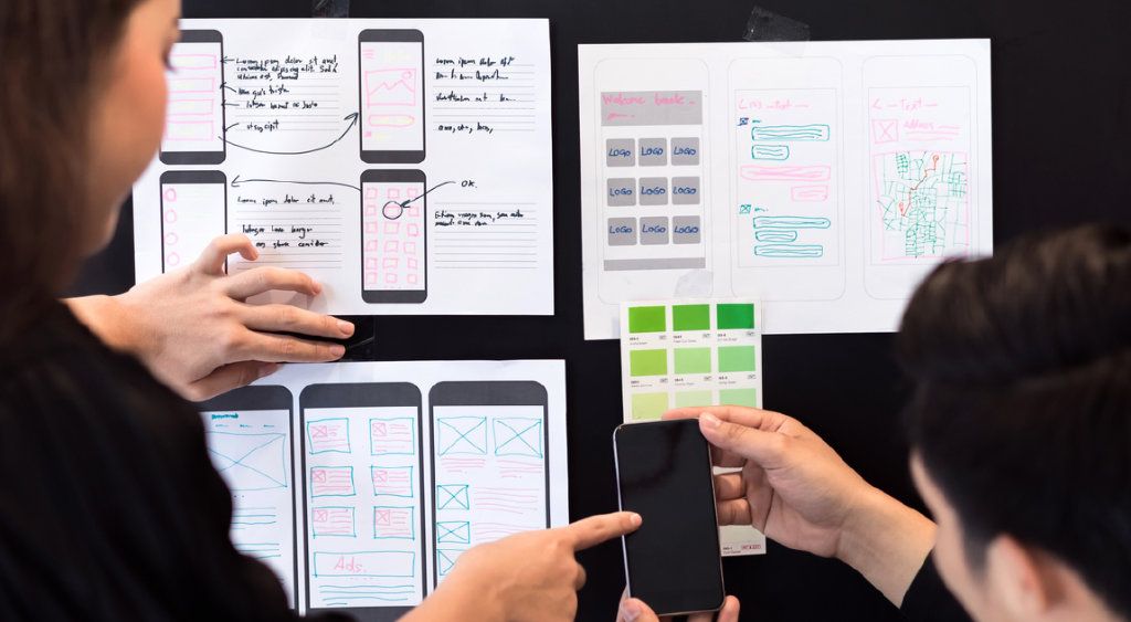 A team arranging paper sketches and sticky notes on a board