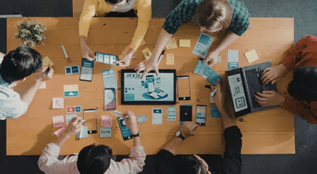 Overhead view of a team planning around a table with laptops and sticky notes